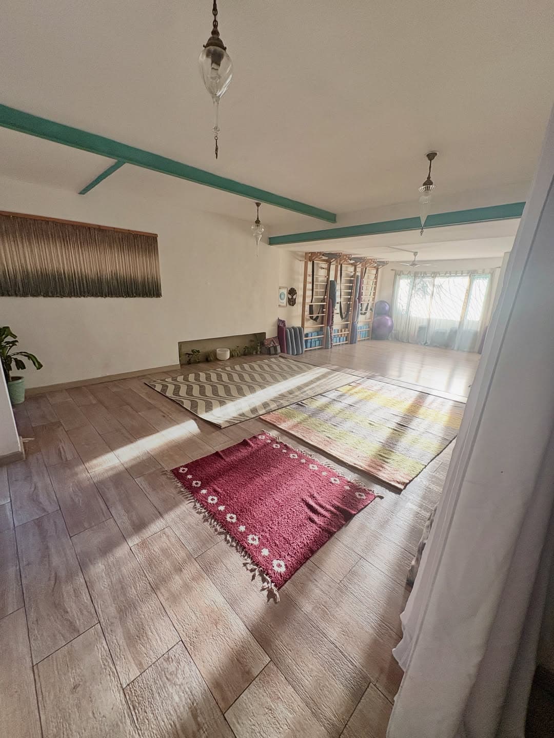 Sala de práctica con tapiz de macramé, plantas y alfombras iluminadas por la luz natural