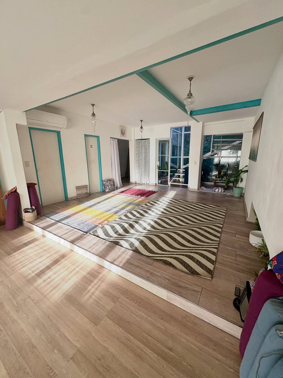 Sala de práctica de is con vigas turquesa, alfombras y luz natural sobre el piso de madera